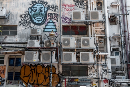 A building's exterior is crowded with air conditioning units, pipes and graffiti.