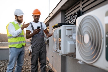 Two technicians work on air conditioning units.