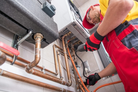 A tradesman repairs the copper pipes of a home boiler.