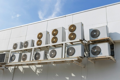 Several commercial HVAC units are mounted on a rack against a white building