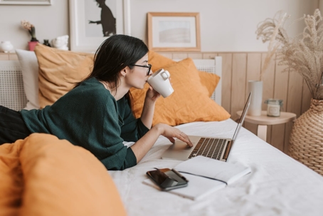 A woman is working on a laptop in bed.
