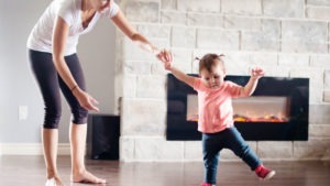 A parent assists a toddler in taking their first steps