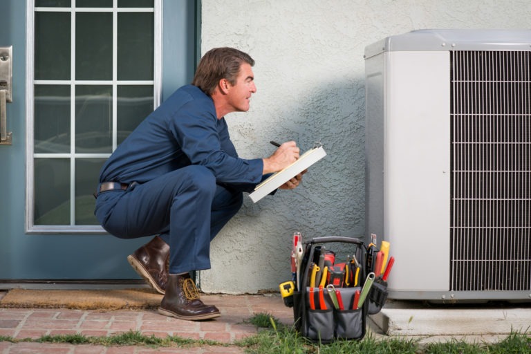 A technician performs maintenance on an outside AC unit